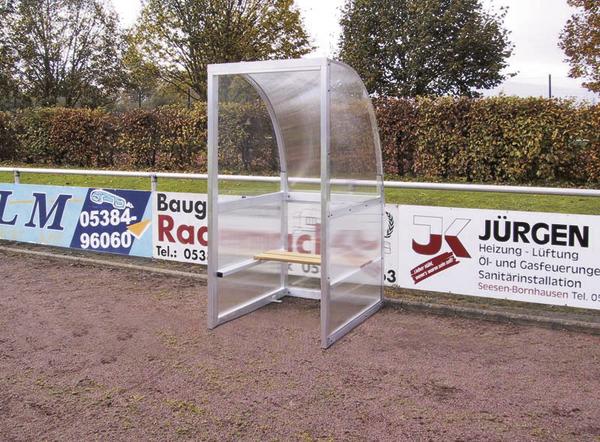 Transparentes Spielertunnel-Schutzhaus am Spielfeldrand mit Werbebannern im Hintergrund.