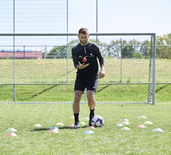 Fußballspieler beim Koordinations- und Reaktionstraining mit Ball auf dem Sportplatz.