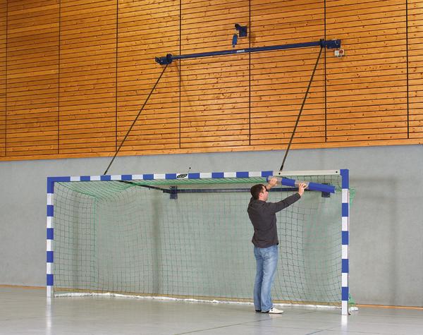 Mann montiert Handballtor in Sporthalle mit Holzwand und grauem Boden.