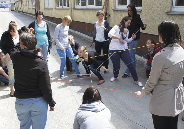 Gruppenspiel mit Menschen, die bunte Fäden im Freien halten und vernetzen.