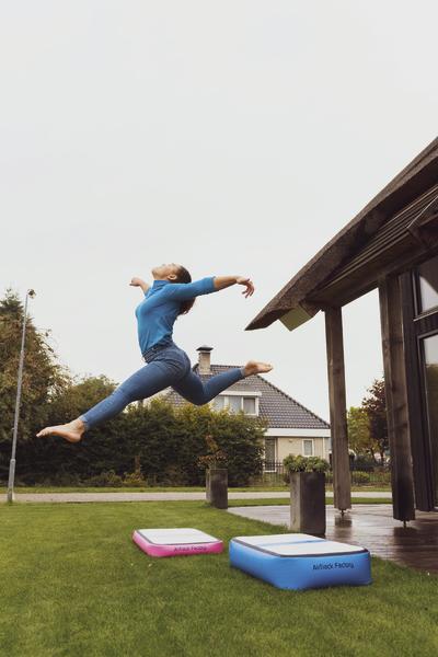 Frau springt im Garten über aufblasbare Airtrack-Matten vor einem modernen Haus.