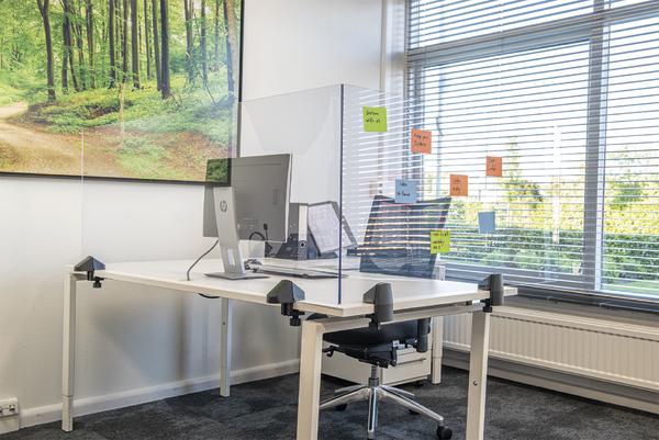 Moderner Büroarbeitsplatz mit Computer, Trennwand und Fenster mit Post-its im Tageslicht.