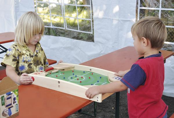 Kinderspiel: Zwei Kinder spielen Tischfußball auf einem Holztisch im Freien.