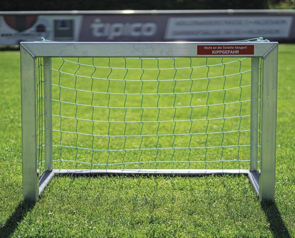 Kleines Fußballtor mit grünem Netz auf Rasenplatz, Warnhinweis wegen Kippgefahr.