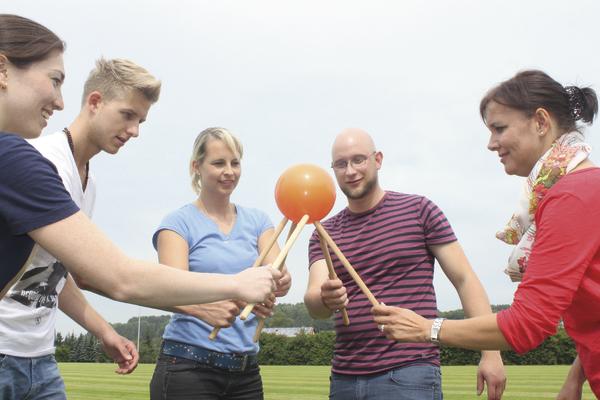 Fünf Personen spielen draußen mit einem orangefarbenen Ball und Stöcken in der Hand.