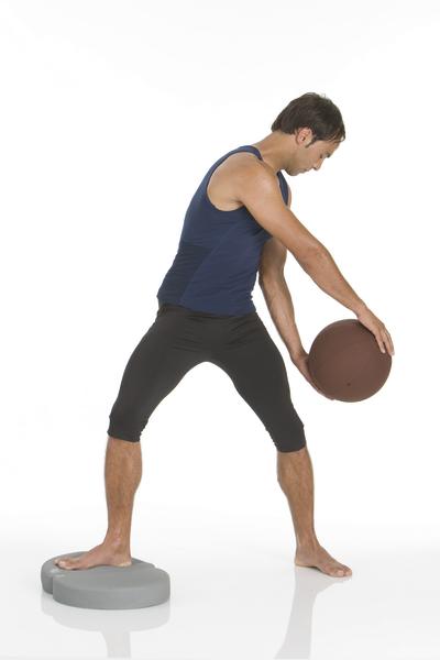 Mann trainiert Gleichgewicht mit Medizinball auf Balancekissen in Sportbekleidung.