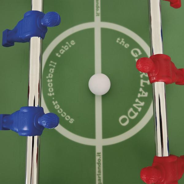 Tischfußball-Spielfeld von oben mit weißem Ball in der Mitte, flankiert von blauen und roten Spielerfiguren an den Metallstangen.