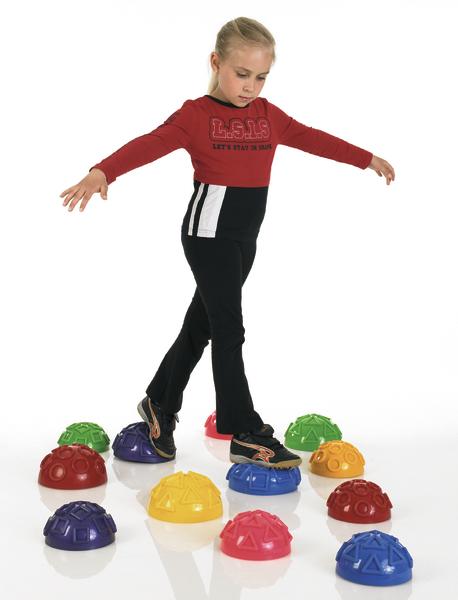 Kind balanciert auf bunten Halbkugeln als Motorikspielzeug auf weißem Hintergrund.