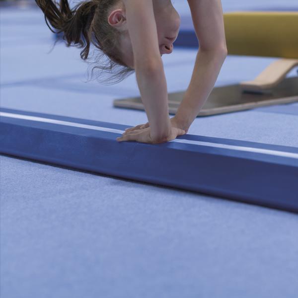 Mädchen macht Handstand auf Schwebebalken in Turnhalle mit blauem Boden.
