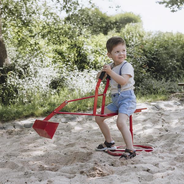 Kleiner Junge spielt mit rotem Sandbagger im Sandkasten an sonnigem Tag im Park.