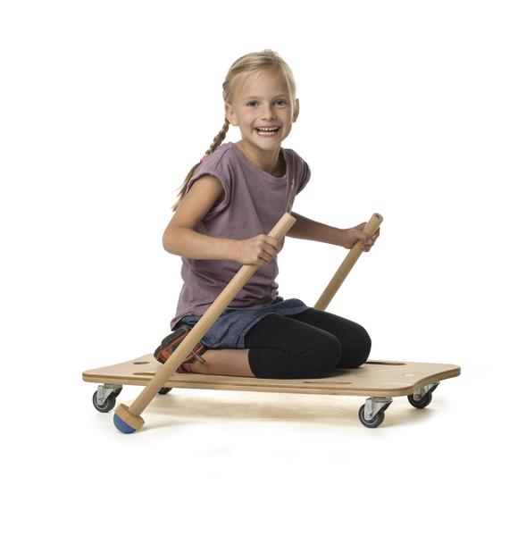 Mädchen sitzt auf Holzroller mit Rollen und hält zwei Holzstöcke zum Fahren, weißer Hintergrund.