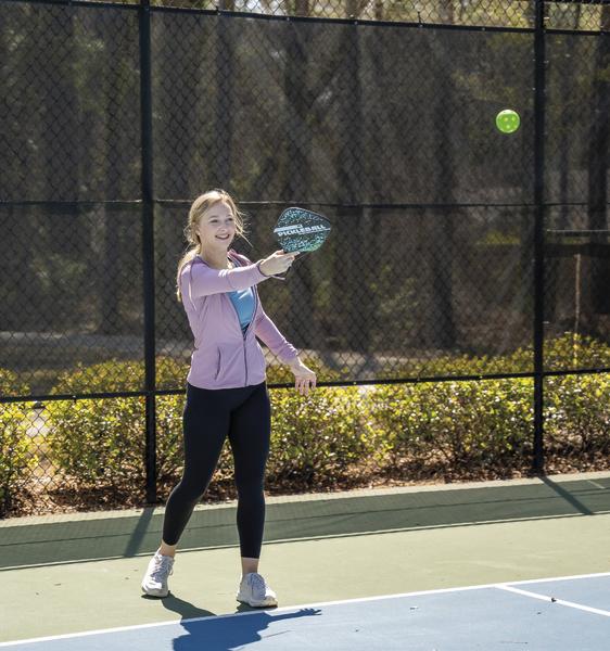 Mädchen spielt mit einem Schläger und grünem Ball auf einem Tennisplatz im Freien.