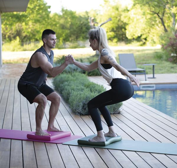 Mann und Frau trainieren zusammen auf Airex Balance Pads draußen.