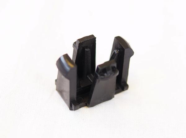 Schwarzes Kunststoffclip-Bauteil mit vier aufrechten Halterungen auf weißem Hintergrund.