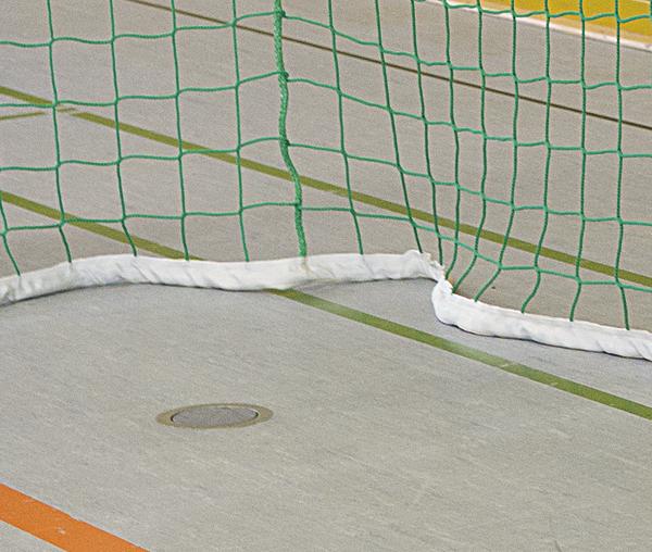 Handballtor mit grünem Netz auf Hallenboden mit Linienmarkierungen.