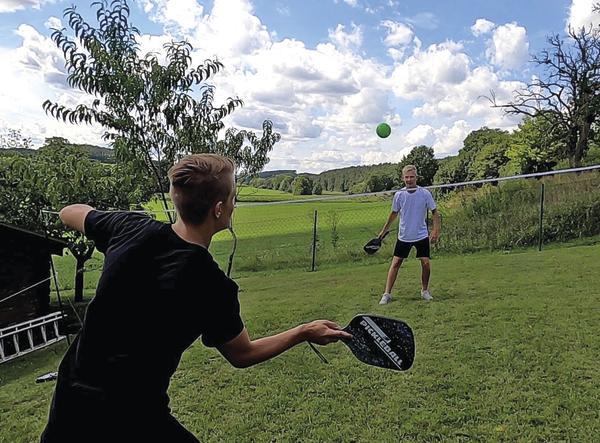 Zwei junge Männer spielen Pickleball im Garten bei sonnigem Wetter.