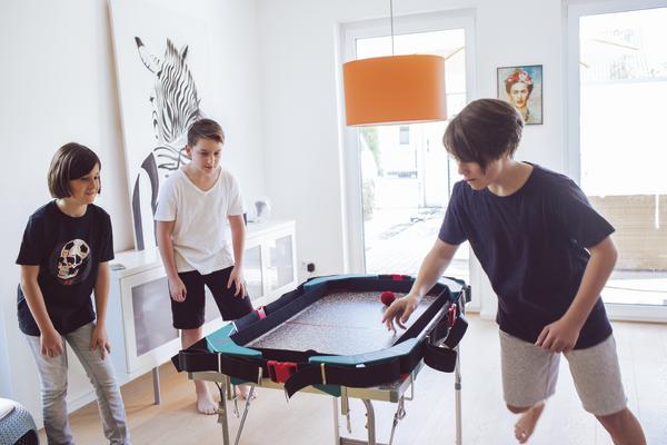 Drei Jungen spielen in einem hellen Wohnzimmer an einem kleinen Billardtisch.