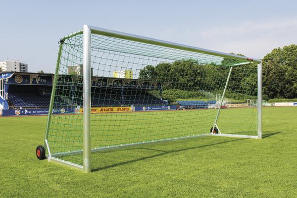 Mobiles Fußballtor mit grünem Netz auf gepflegtem Rasen in einem Stadion bei Sonnenschein.