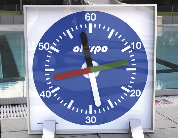 Großes Schwimmstoppuhr mit blauem Zifferblatt und farbigen Zeigern am Schwimmbeckenrand.