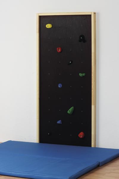 Kletterwand mit bunten Griffen und blauer Matte in Innenraum, ideal für Kinder und Training.