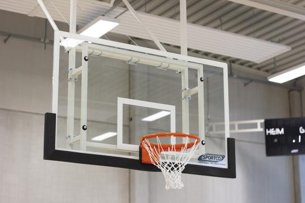 Basketballkorb mit orangefarbenem Ring und weißem Netz in einer Sporthalle.