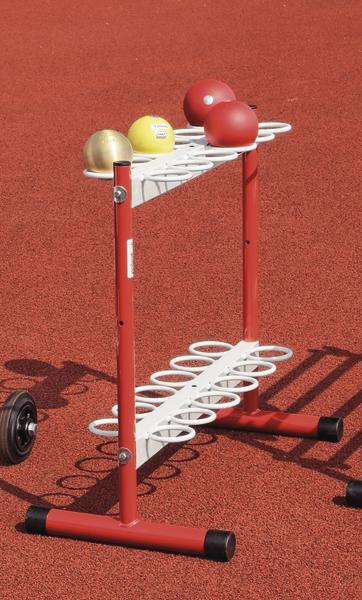 Roter Kugelhalter mit Kugeln auf rotem Sportplatzboden, bereit für Kugelstoß-Wettbewerb.