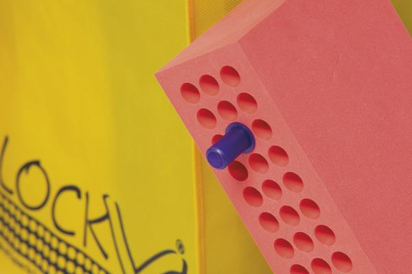 Roter BlockX®-Block mit blauem Stecker vor gelbem Sack mit Logo.