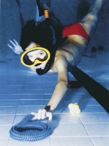 Kind mit Schnorchelmaske und roter Badehose taucht im Pool und greift nach einem Spielzeugring.