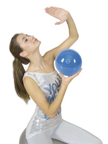 Frau in Sportkleidung hält blauen Gymnastikball und macht Dehnübung auf Gymnastikball.