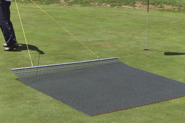 Golfplatz mit Rasenrechen zum Ebnen des Grüns, zwei Personen ziehen das Gerät über das Gras.