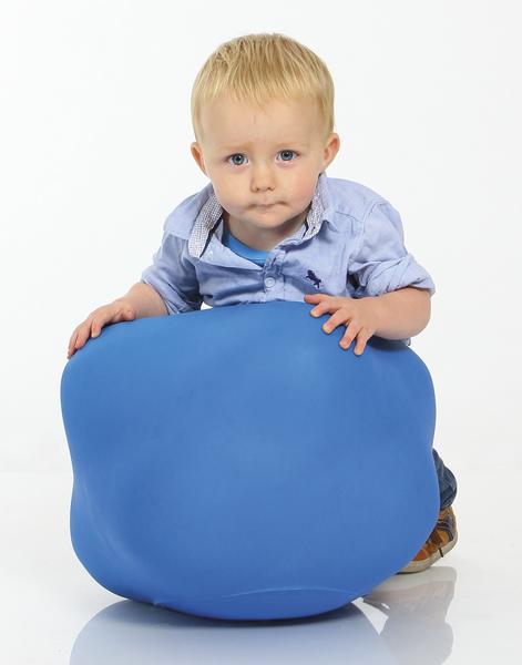Kleiner Junge in blauem Hemd spielt mit großem blauen Ball auf weißem Hintergrund.