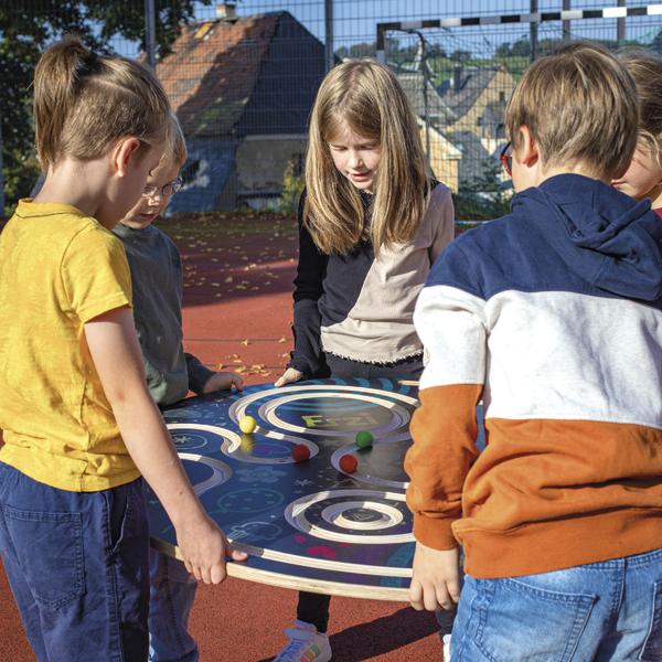 Kinder spielen gemeinsam ein Geschicklichkeitsspiel mit bunten Kugeln auf einem Outdoor-Spielbrett.