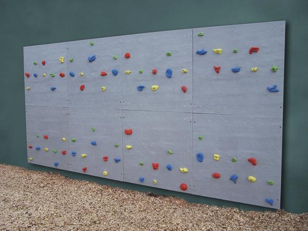 Kletterwand mit bunten Griffen an grauer Wand, Outdoor-Spielplatz mit Fallschutzboden.