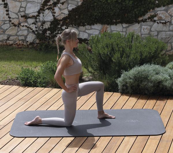 Frau bei einer Dehnübung auf einer grauen AIREX Gymnastikmatte im Freien.