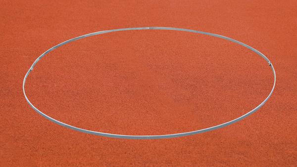 Roter Sportplatz mit markiertem Kreis für Kugelstoßen oder Diskuswurf.