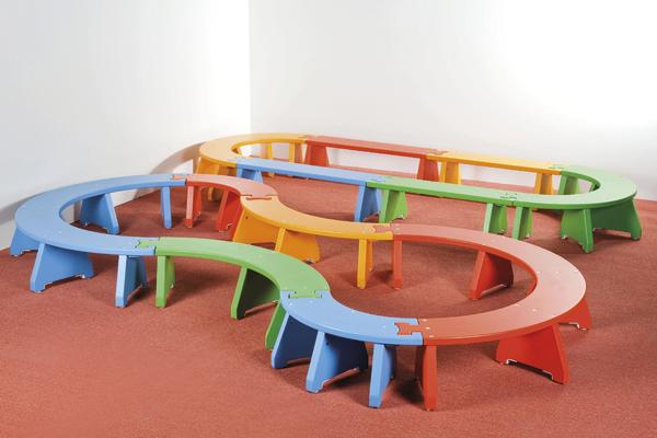 Bunte, geschwungene Sitzbänke aus Holz auf rotem Teppich in einem weißen Raum.