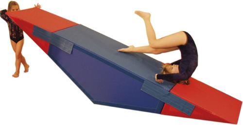 Kind turnt auf rotem und blauem Schrägbrett aus Schaumstoff im Turnanzug.