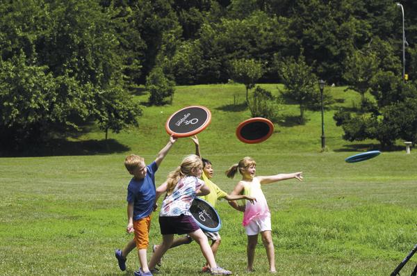 Kinder spielen im Park mit bunten Frisbees auf einer grünen Wiese bei Sonnenschein.