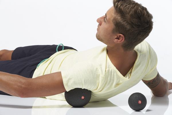 Mann liegt seitlich und nutzt einen Massageball zur gezielten Behandlung der Rückenmuskulatur, während ein weiterer Ball daneben liegt.