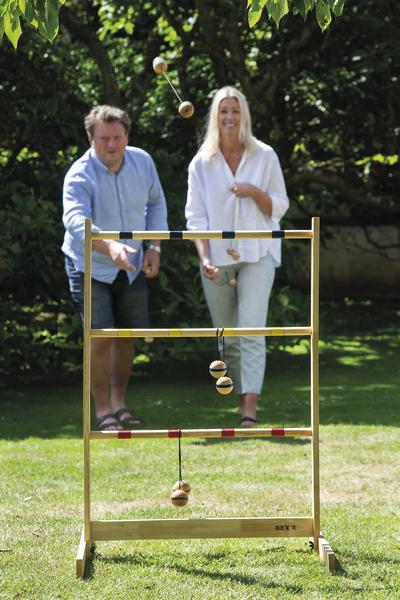 Zwei Personen spielen im Garten ein Wurfspiel mit hängenden Holzkugeln an einem Gestell.