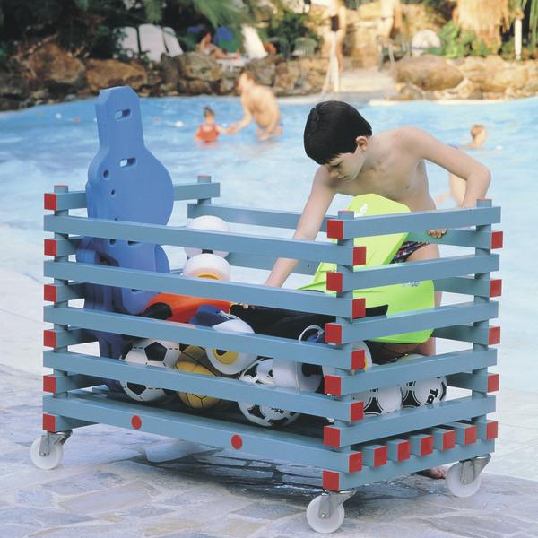 Kind greift in blauen Wagen mit Sportbällen am Poolrand, andere Kinder im Wasser.