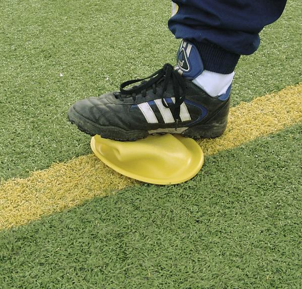 Fuß mit Fußballschuh auf gelber Trainingsmarkierung auf Kunstrasenplatz.
