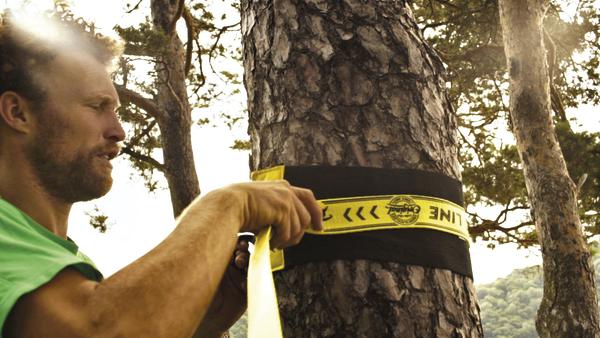 Mann spannt Slackline an Baum im Wald für Outdoor-Sport und Balance-Training.
