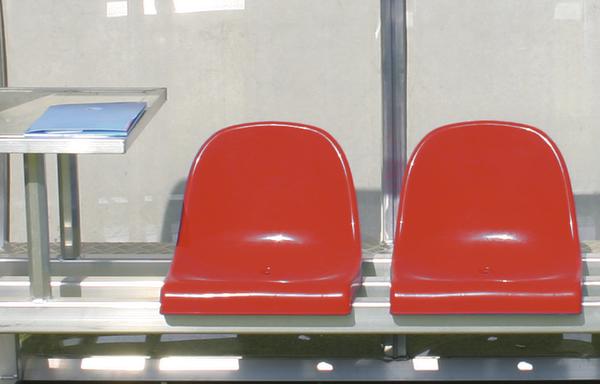 Zwei rote Kunststoffsitze auf Metallbank.