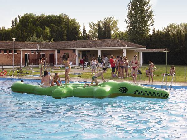 Kinder spielen auf einem grünen Krokodil-Wasserfloß im Schwimmbad an einem sonnigen Tag.