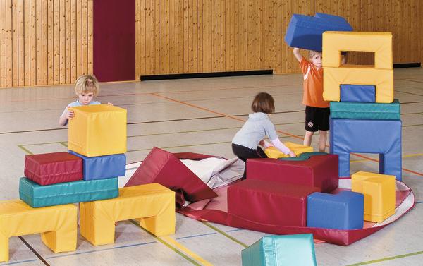 Kinder spielen mit bunten Schaumstoffbausteinen in einer Turnhalle.