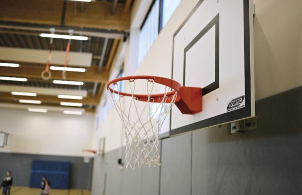 Basketballkorb mit rotem Ring und weißem Netz in einer Sporthalle, Nahaufnahme.