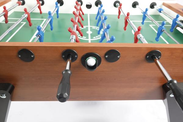 Tischkicker mit roten und blauen Spielfiguren und weißem Ball auf grünem Spielfeld.