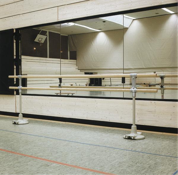 Ballettstudio mit Spiegelwand und Holz-Ballettstangen auf Sporthallenboden.