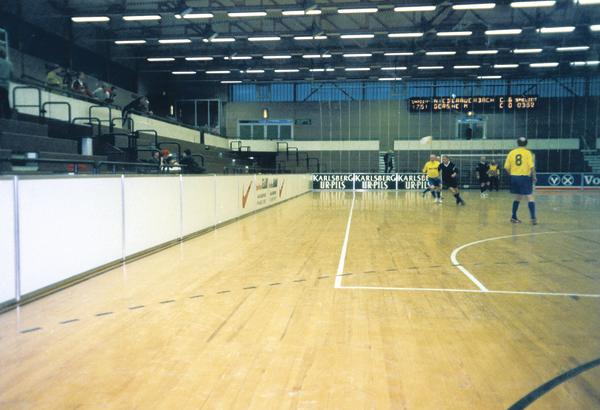 Hallenfußballspiel in einer Sporthalle mit Spielern in gelben Trikots und digitaler Anzeigetafel.